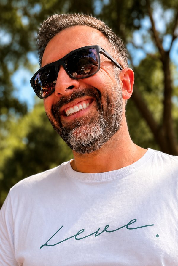 Foto do Eric de Castro sorrindo, de óculos escuros, ao ar livre.